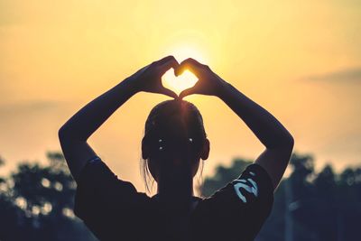 Rear view of woman making heart shape with hands against sky during sunset