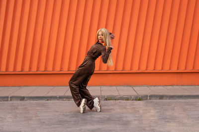Cheerful african american woman in sportswear dancing in the street on an orange background