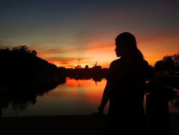 Silhouette woman standing by lake against sky during sunset