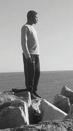 Woman standing on rock by sea against clear sky