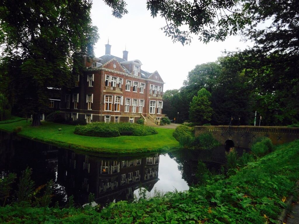 architecture, building exterior, built structure, tree, green color, growth, house, reflection, water, sky, city, outdoors, residential building, day, plant, residential structure, no people, travel destinations, building, clear sky