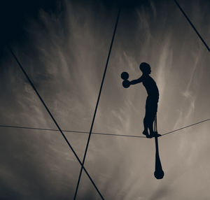 Silhouette man balancing on tightrope against sky during sunset