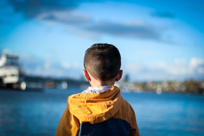 Rear view of boy standing in sea against sky