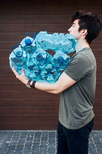 Young man throwing out empty used plastic water bottles into trash bin