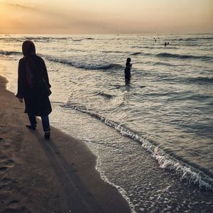 People walking on beach against sky during sunset