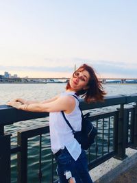 Beautiful woman standing by railing against sea against sky