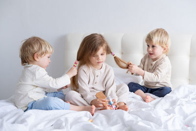 Cute brothers holding sisters hair on bed at home