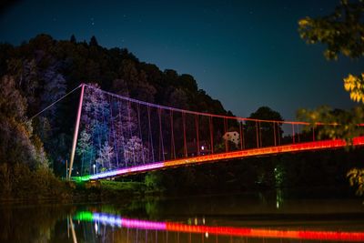 Illuminated bridge over lake against sky at night