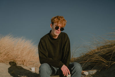 Portrait of young man wearing sunglasses while sitting against clear sky