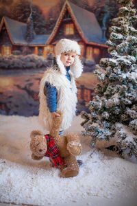 Cute girl holding stuffed toy standing by christmas tree