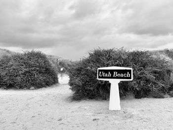 Information sign on road amidst trees against sky