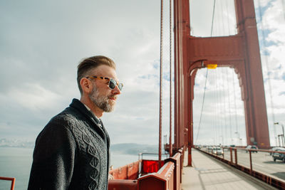 Profile portrait of adult man with beard standing on the golden gate bridge during cloudy weather