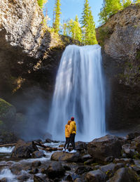 Rear view of man standing against waterfall