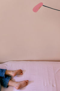 Low section of child relaxing on bed against wall
