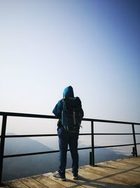 Rear view of man standing by railing against clear sky