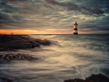 Lighthouse by sea against sky during sunset