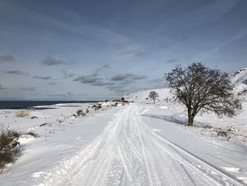Road by snow covered land against sky