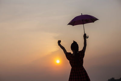 Silhouette man holding umbrella against sky during sunset