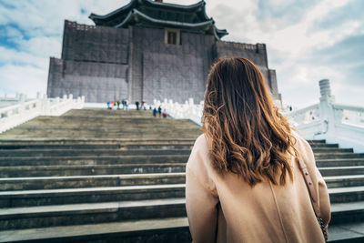 Rear view of tourist standing on staircase while looking at historical building