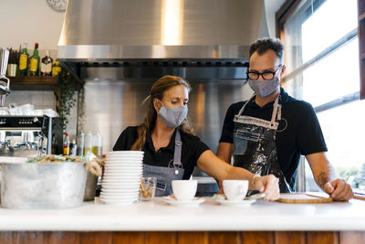 Male and female baristas in protective face mask working at coffee shop during covid-19