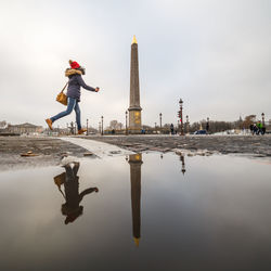 Reflection of woman in puddle against sky