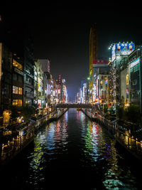 Illuminated buildings by river against sky at night