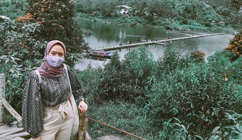 Portrait of young woman in mask standing against lake