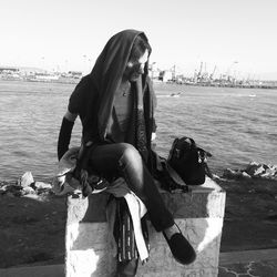 Woman wearing headscarf sitting on retaining wall against sea