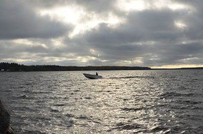 Boat sailing in sea against cloudy sky