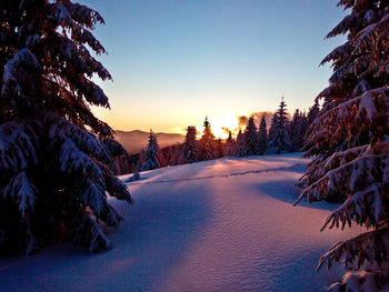 Snow covered landscape against sky during sunset