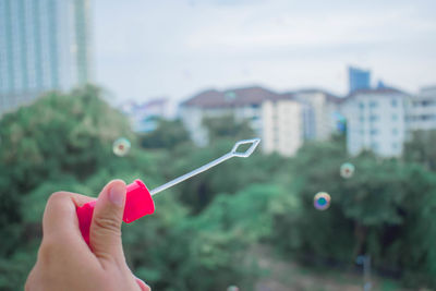 Close-up of hand holding bubble wand against building in city