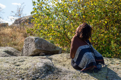 Rear view of woman sitting on rock