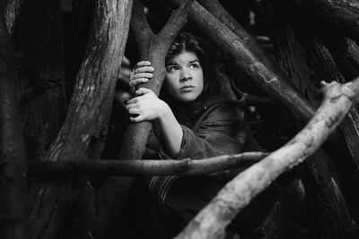 Young woman looking up while hiding behind firewood in forest