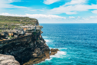 Cliff by sea against cloudy sky