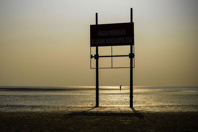 Information sign on beach against sky during sunset