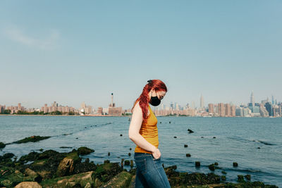 Woman standing by sea against cityscape