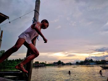 Man jumping in sea against sky during sunset