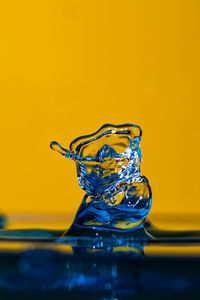 Close-up of water splashing on glass against yellow background