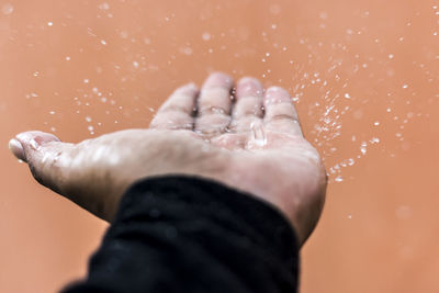 Close-up of water drops falling on hand against wall