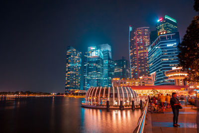 Illuminated buildings by river against sky at night