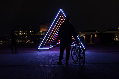 Rear view of silhouette woman walking on illuminated city at night