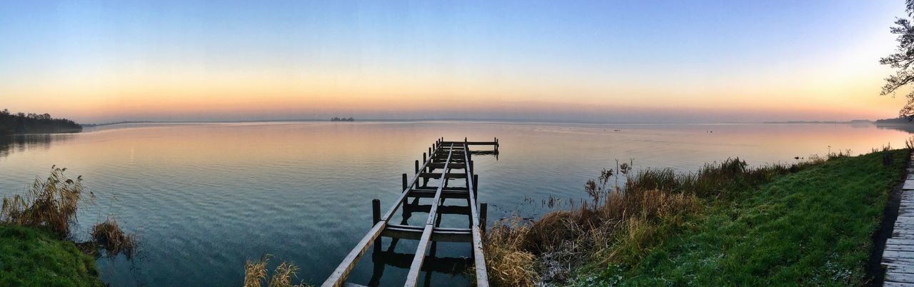 water, clear sky, tranquility, tranquil scene, sunset, copy space, scenics, sea, beauty in nature, blue, nature, reflection, pier, idyllic, lake, horizon over water, jetty, grass, built structure, sky