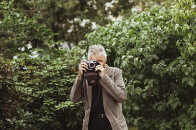 Elderly man photographing through camera against plants in park