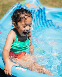 Cute smiling girl sitting in wading pool outdoors