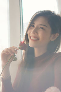 Smiling young woman holding rose while looking away at home