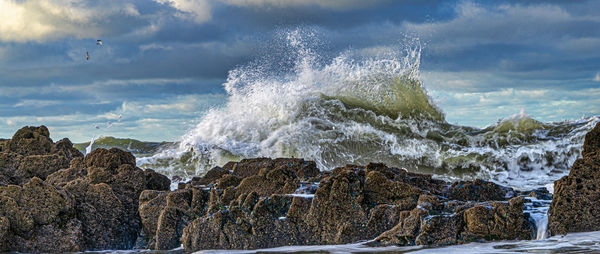 Waves splashing on rocks at shore against sky