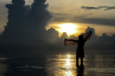 Silhouette girl standing in sea against sky during sunset