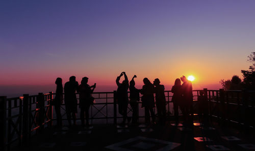 Silhouette people standing by railing against sky during sunset