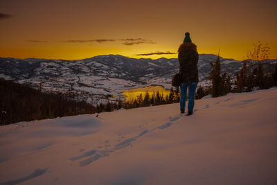 Rear view of person standing on snowcapped mountain against sky during sunset