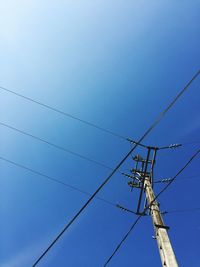 Low angle view of electricity pylon against clear blue sky